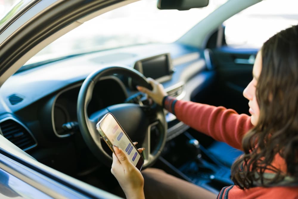 Female teenage driver using a smartphone while behind the wheel, highlighting the dangers of distracted driving and road safety concerns