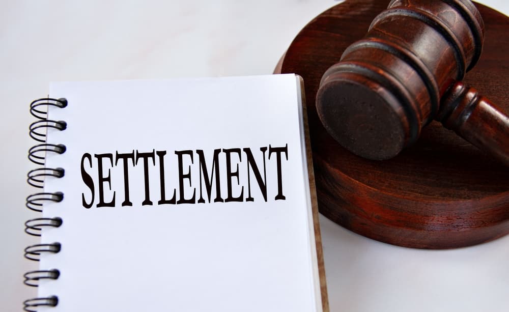 SETTLEMENT - word in a white notebook with a judge's gavel in the background