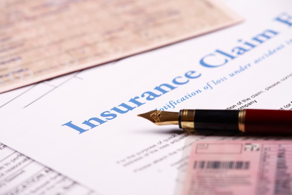 Blank insurance claim form and other papers like ID or vehicle documents and pen lying on desk