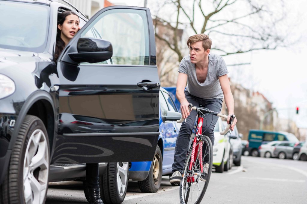 Cyclist nearly hit by car door opening on street, showing risk of bicycle dooring accidents.