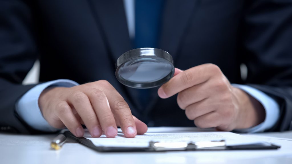 Businessman examining legal documents with a magnifying glass for investigation or contract review.