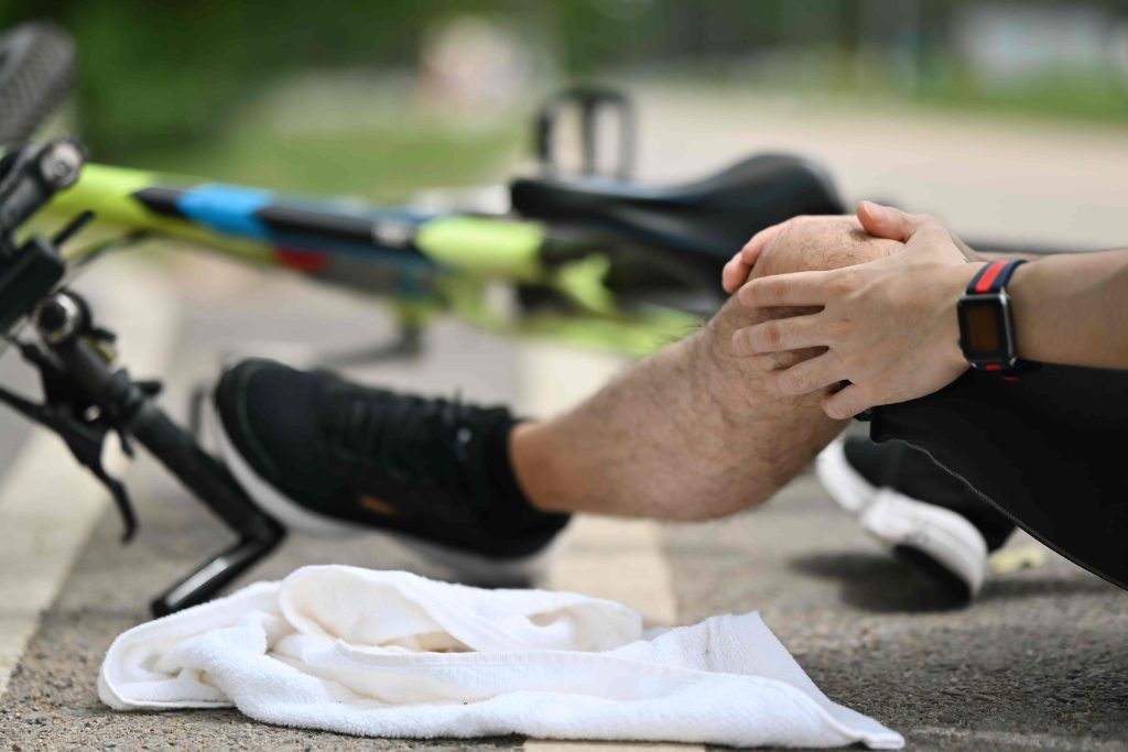 Cyclist sitting on the ground holding injured knee after bicycle accident.