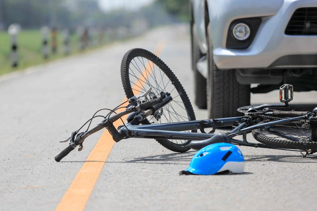 Bicycle accident on the road with a car, showing fallen bike and helmet in front of vehicle.