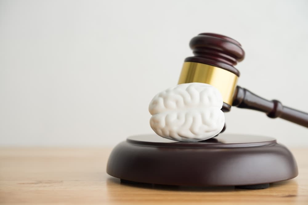 Judge’s gavel resting on a small model of a human brain on a wooden table.