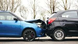 A blue car rear-ended a black car on a road, showing visible front-end and rear-end damage, illustrating a typical rear-end collision accident scene.