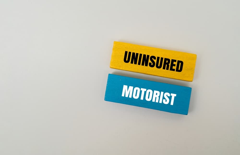 Two colored wooden blocks on a light background — one yellow block with the word ‘UNINSURED’ and one blue block with the word ‘MOTORIST’ — representing the concept of an uninsured motorist.
