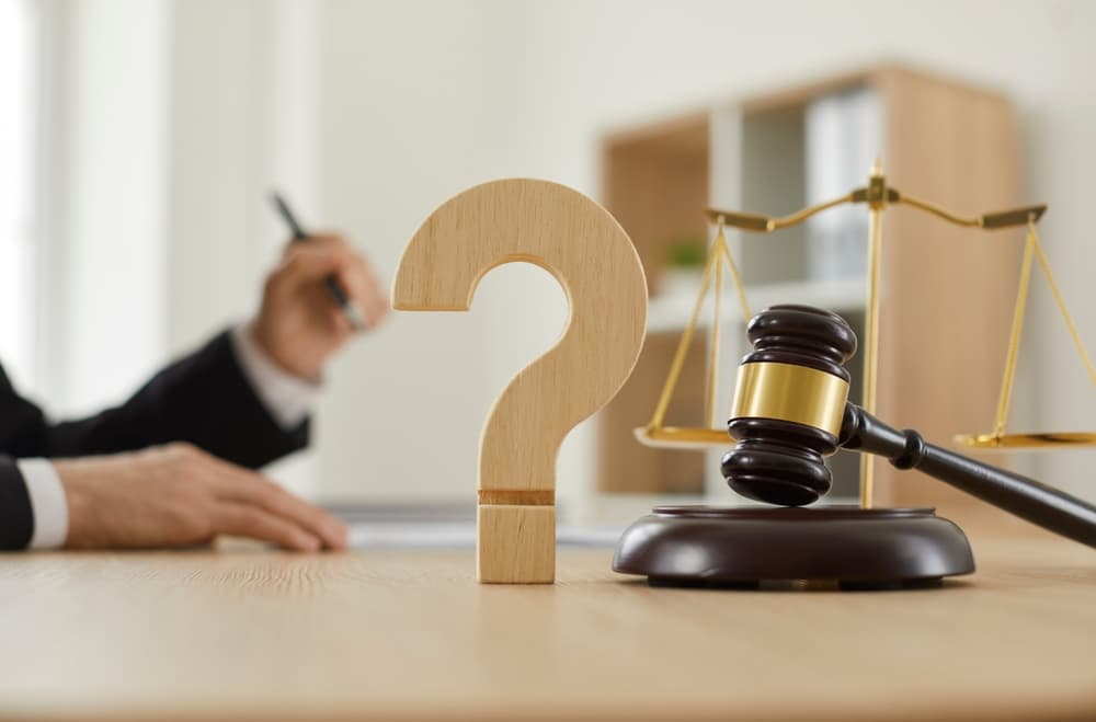 Wooden question mark beside a judge&rsquo;s gavel and scales of justice on a lawyer&rsquo;s desk, symbolizing legal advice and questions to ask an attorney.