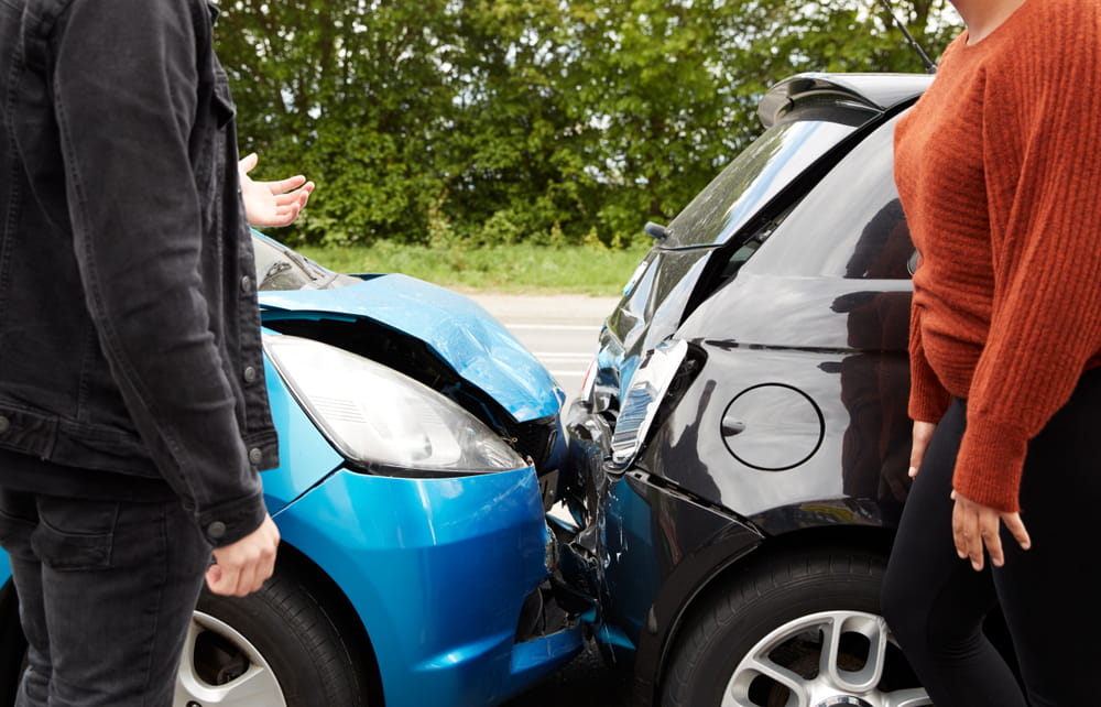 Drivers standing near two damaged vehicles after a crash, discussing accident liability and insurance claims.